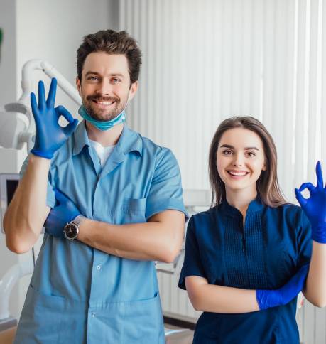 Photo of smiling dentist standing with arms crossed with her colleague, showing okay sign.